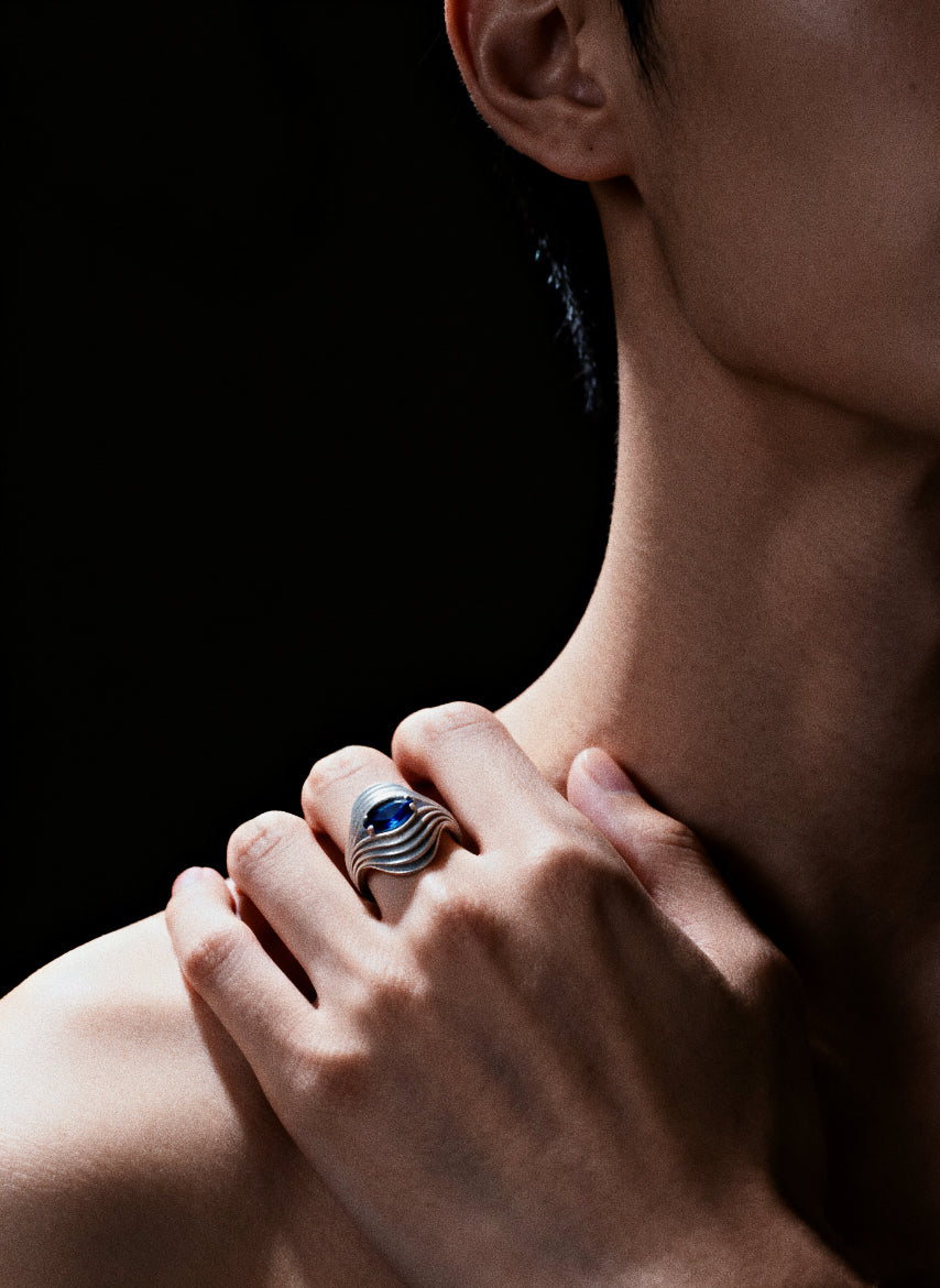 Eye of the Nebula · Sapphire & Silver Ring — Close-up of a person wearing a ring with a blue gemstone on a dark background