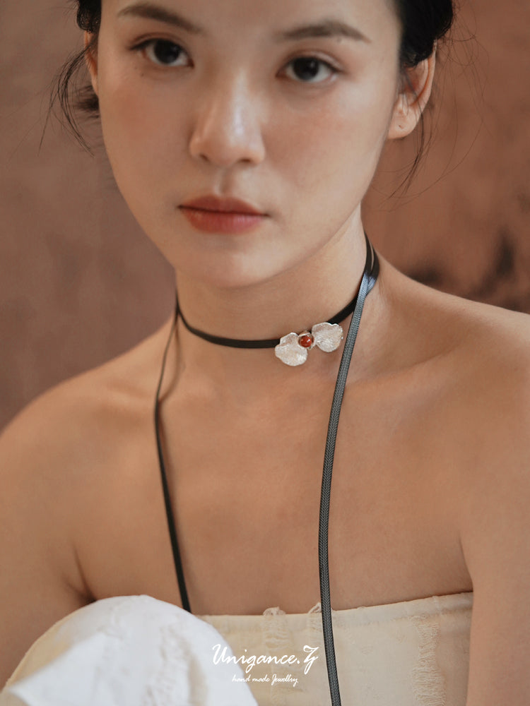 Woman wearing a delicate necklace with a floral pendant against a brown background