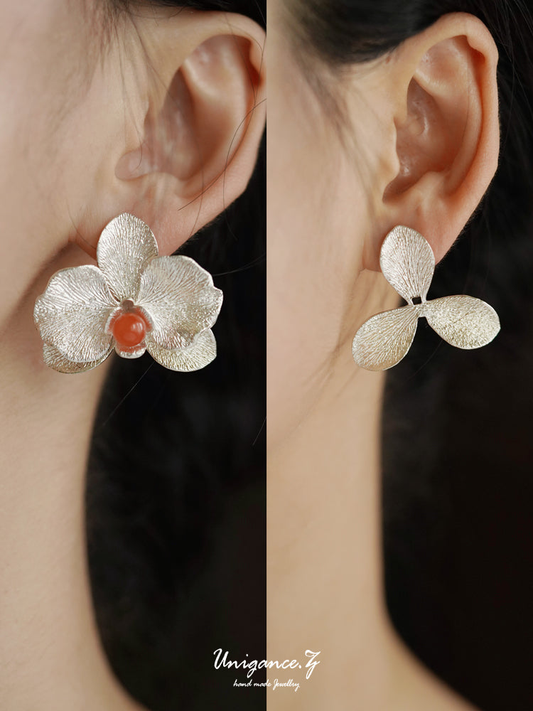 Silver flower-shaped earrings with a red center worn by a person against a dark background.