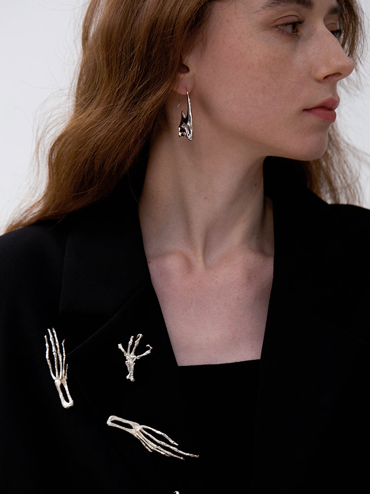 Close-up of a person wearing silver skeleton hand earrings with a black top featuring skeleton designs.