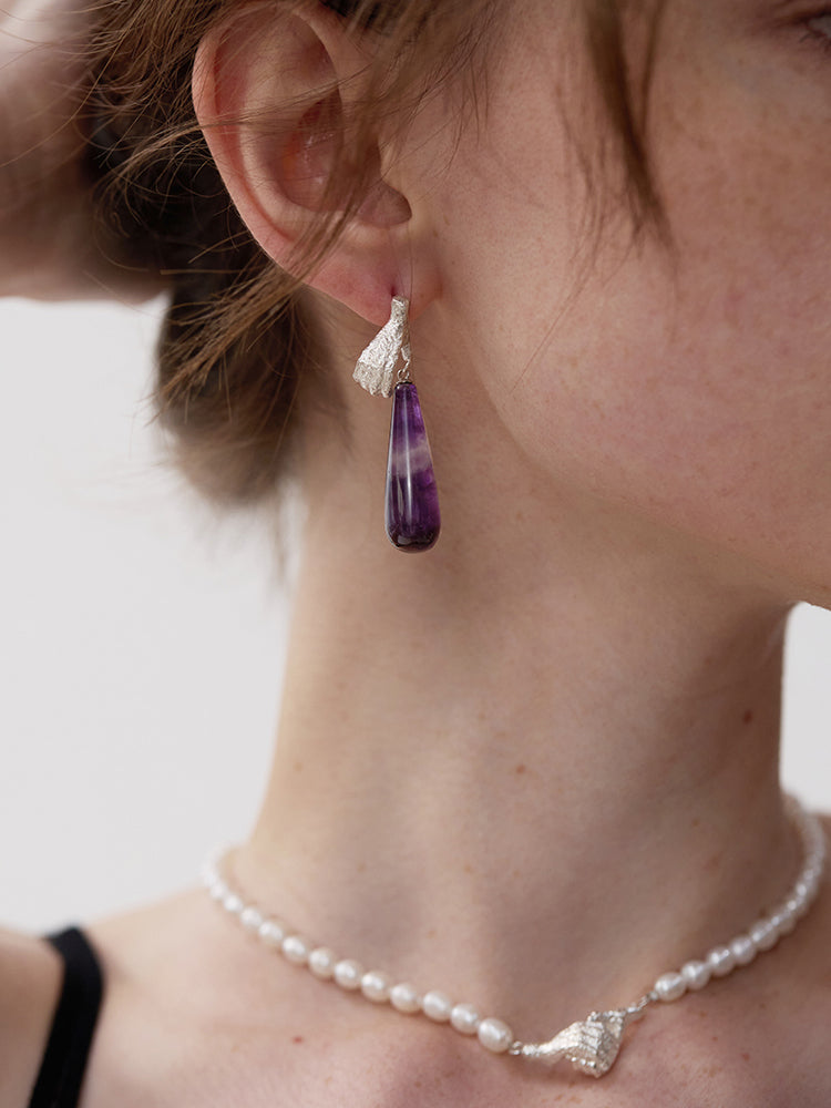 Gold Digger · Gemstones Teardrop Earrings — Close-up of a person wearing a purple teardrop earring and pearl necklace.