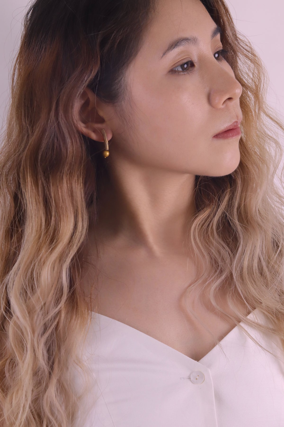 Golden Orchid Lacquer Quasi-Maki-e Earrings — Woman with wavy hair wearing a white top against a plain background