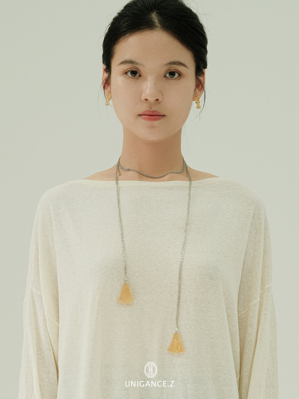 Woman wearing a long necklace with a pendant against a plain background