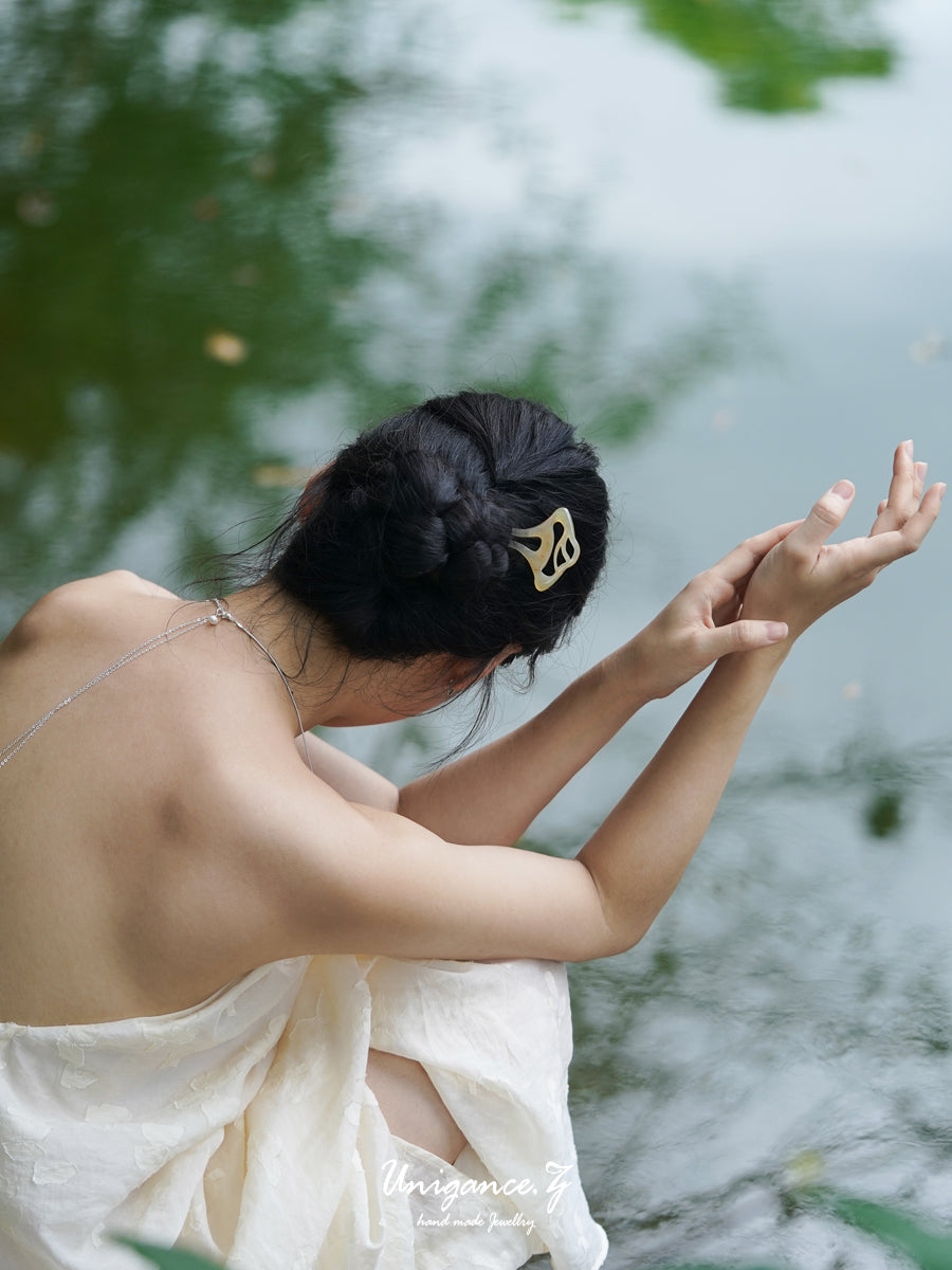 Woman with a hair clip sitting by a body of water, wearing a white dress.