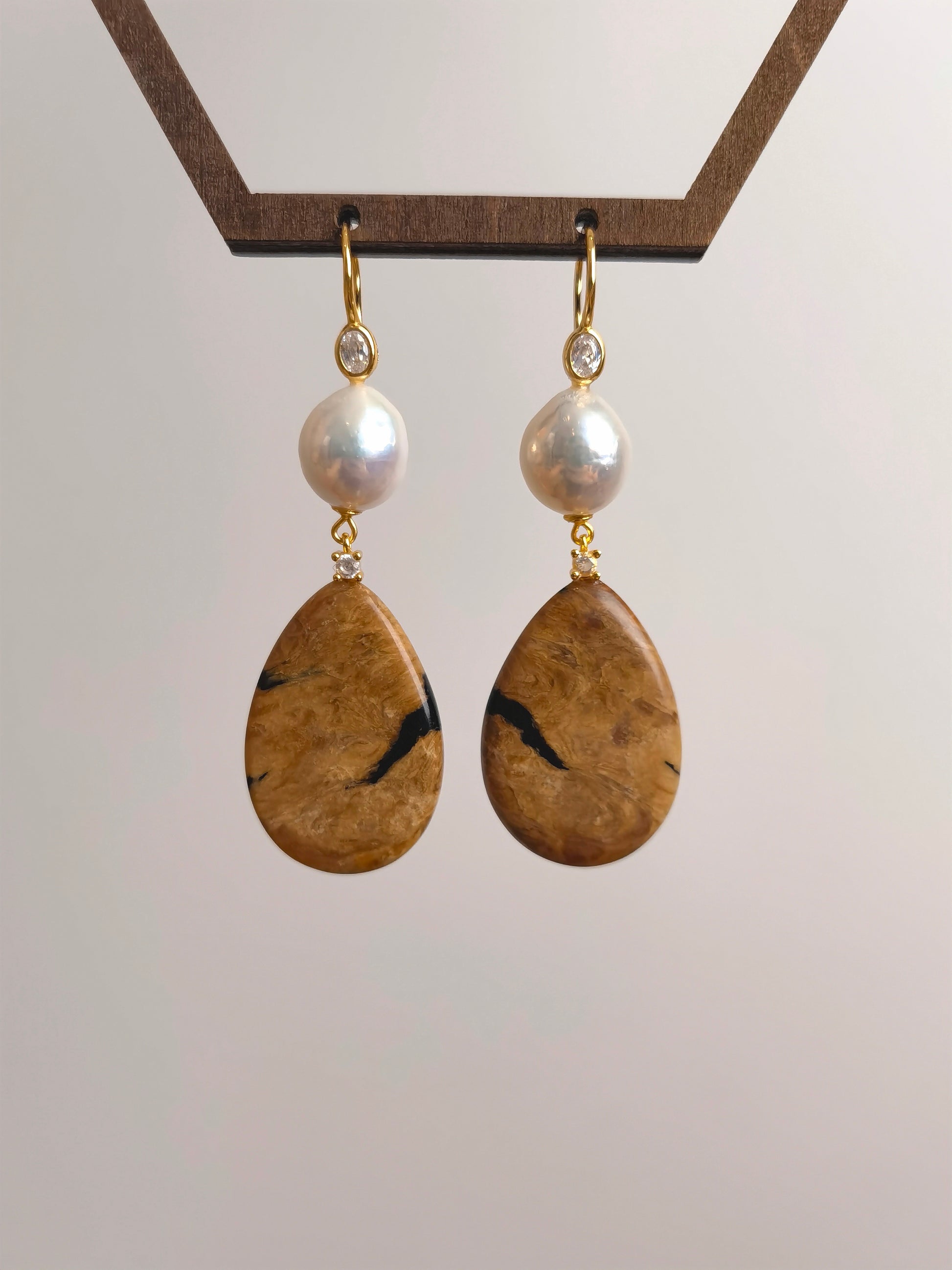 Pair of earrings with teardrop-shaped stones and pearl beads on a light gray background