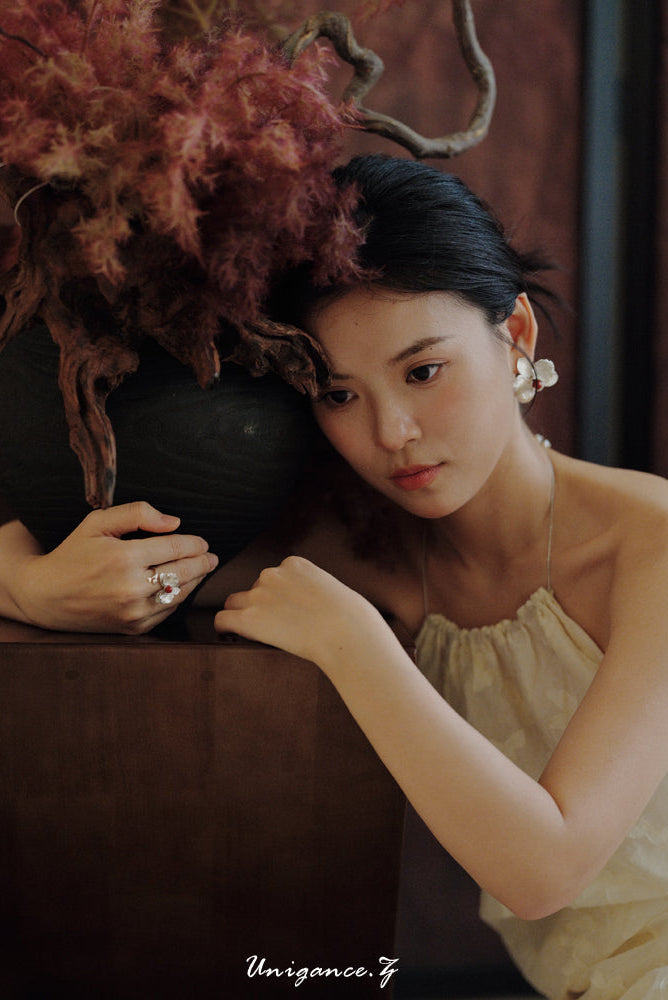 Woman in a beige dress sitting next to a decorative plant with a blurred background
