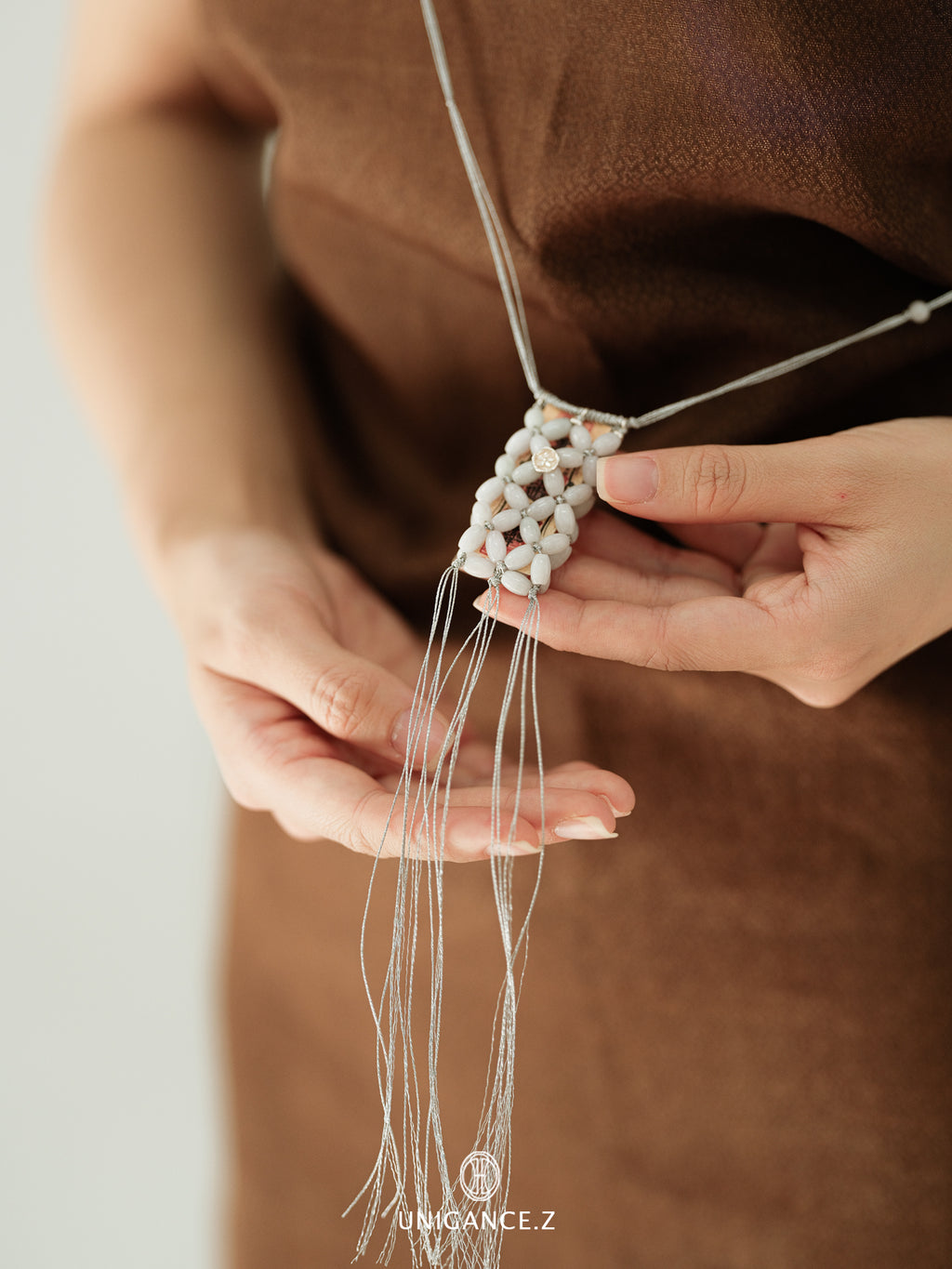 Person holding a delicate necklace with intricate design against a neutral background