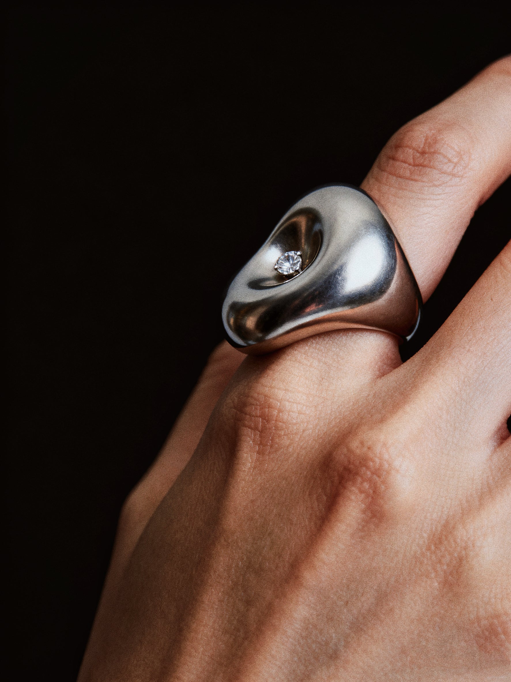 Silver ring with a diamond on a hand against a black background