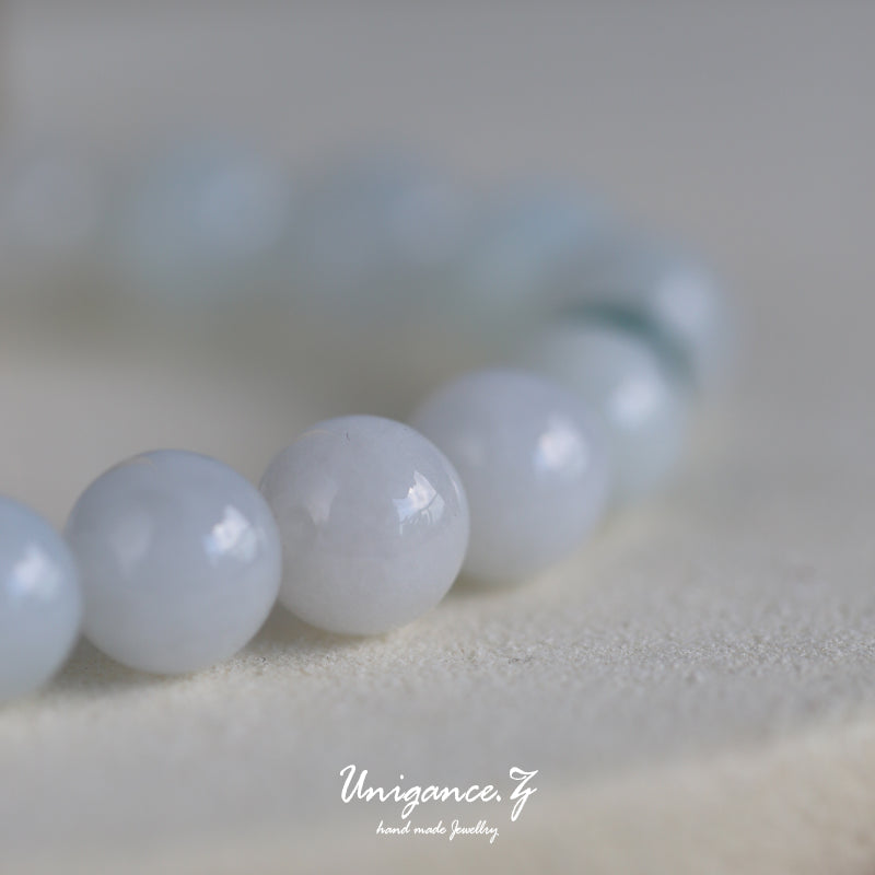Close-up of a bracelet with light blue beads on a neutral background, featuring the brand 'Unigance'.