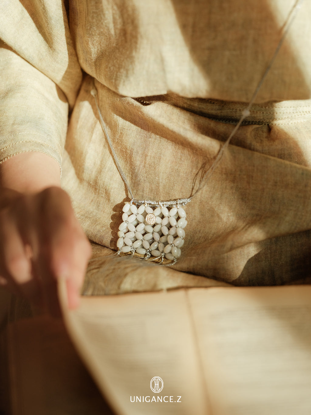 Jade Beaded Pouch — Close-up of a beige fabric with a decorative white pattern, featuring the brand 'UNIGANCE'.