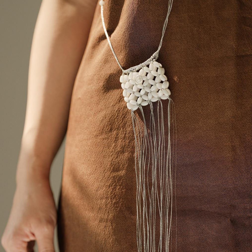 Necklace with white beads and long strands hanging on a brown background