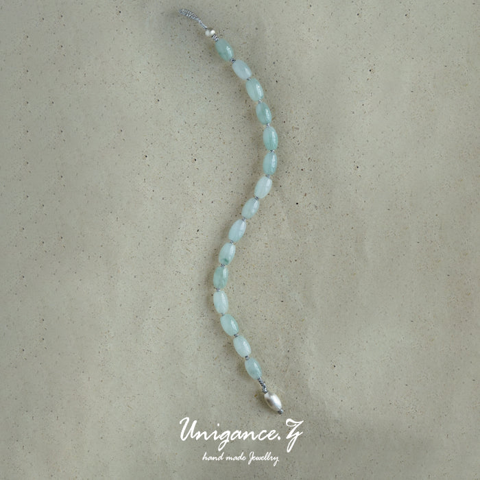 Jade Rice Bead Bracelet — Beaded necklace on a textured beige background with 'Unigance' branding.