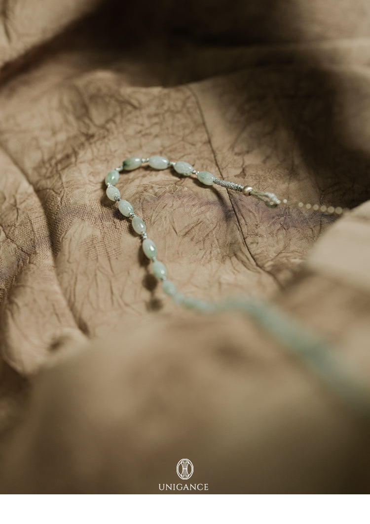 Jade Rice Bead Layered Necklace — Delicate beaded bracelet on a textured surface with 'UNIGANCE' branding.