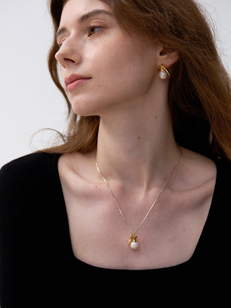 Last Gift Grenade Pearl — Woman wearing a gold necklace with a pearl pendant against a neutral background
