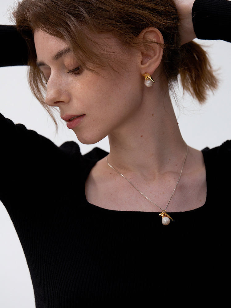 Last Gift · Grenade Pearl Stud Earrings — Woman wearing a gold earring and necklace with pearl-like pendants on a white