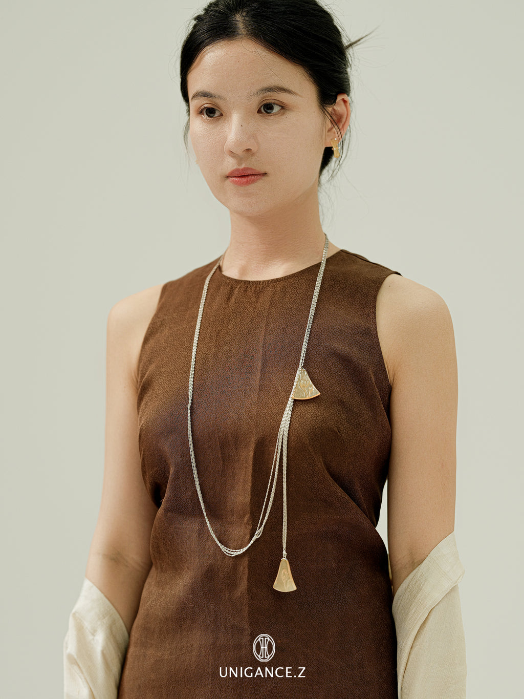 Woman wearing a brown sleeveless top with a long necklace against a plain background