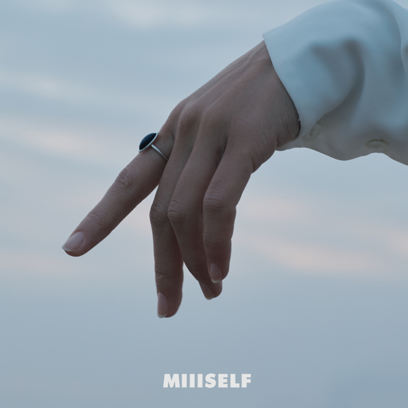 Hand with a ring against a blurred sky background, featuring the brand 'MIIISELF'.