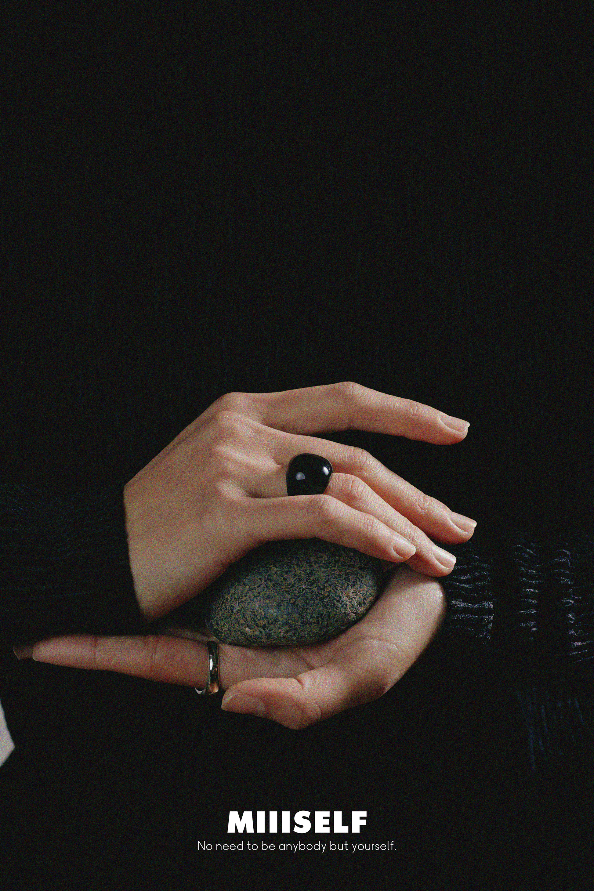 Hand holding a stone with 'MIIISSELF' branding on a black background