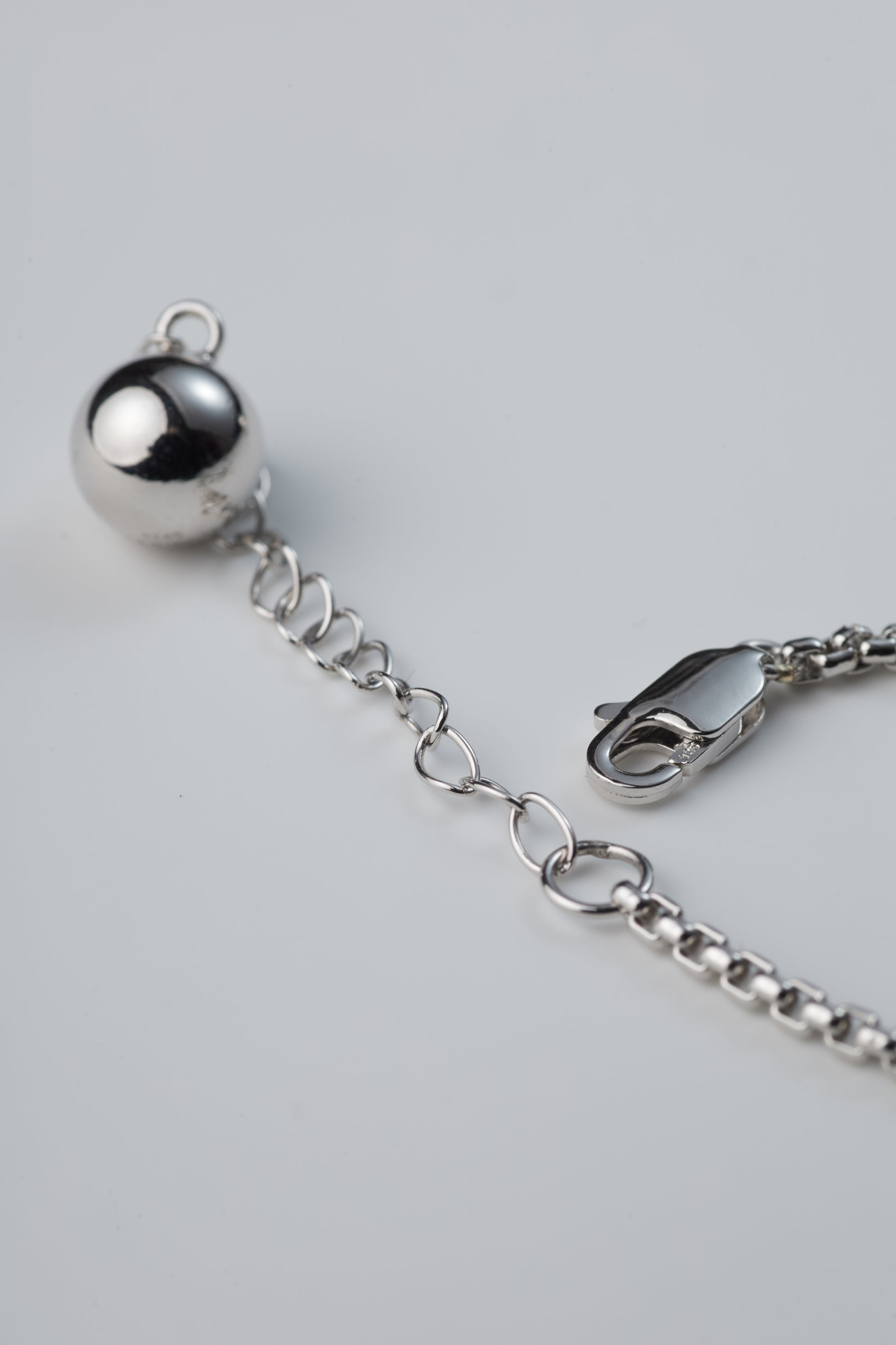 Silver bracelet with a spherical charm on a light gray background