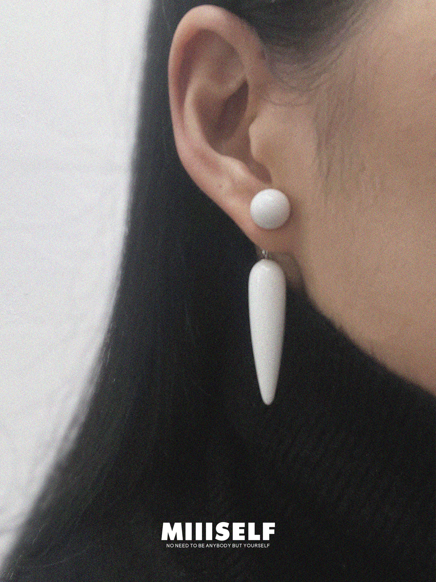 Close-up of an ear wearing a white earring with 'MIISSELF' branding.