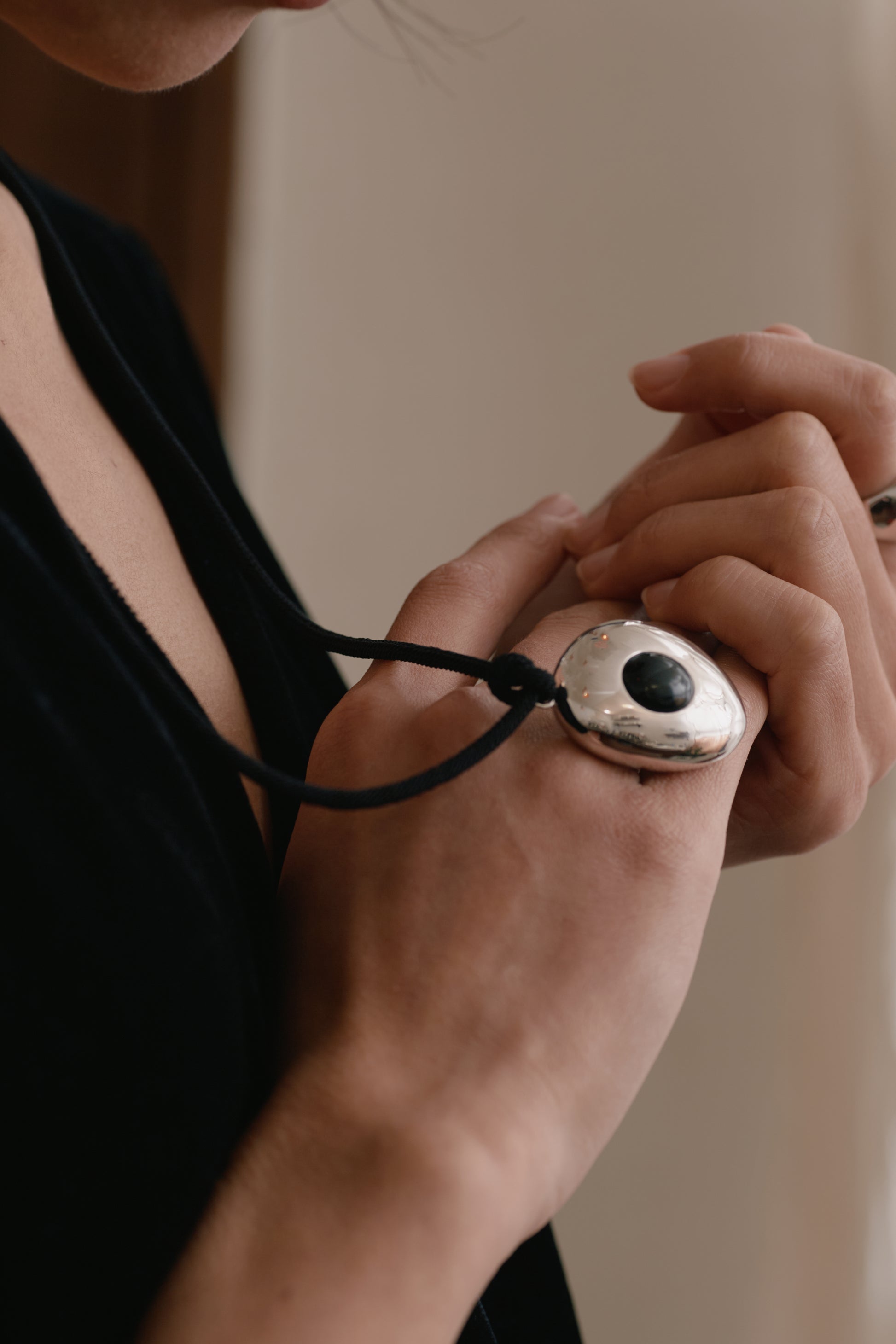 Person holding a necklace with an eye-shaped pendant against a neutral background