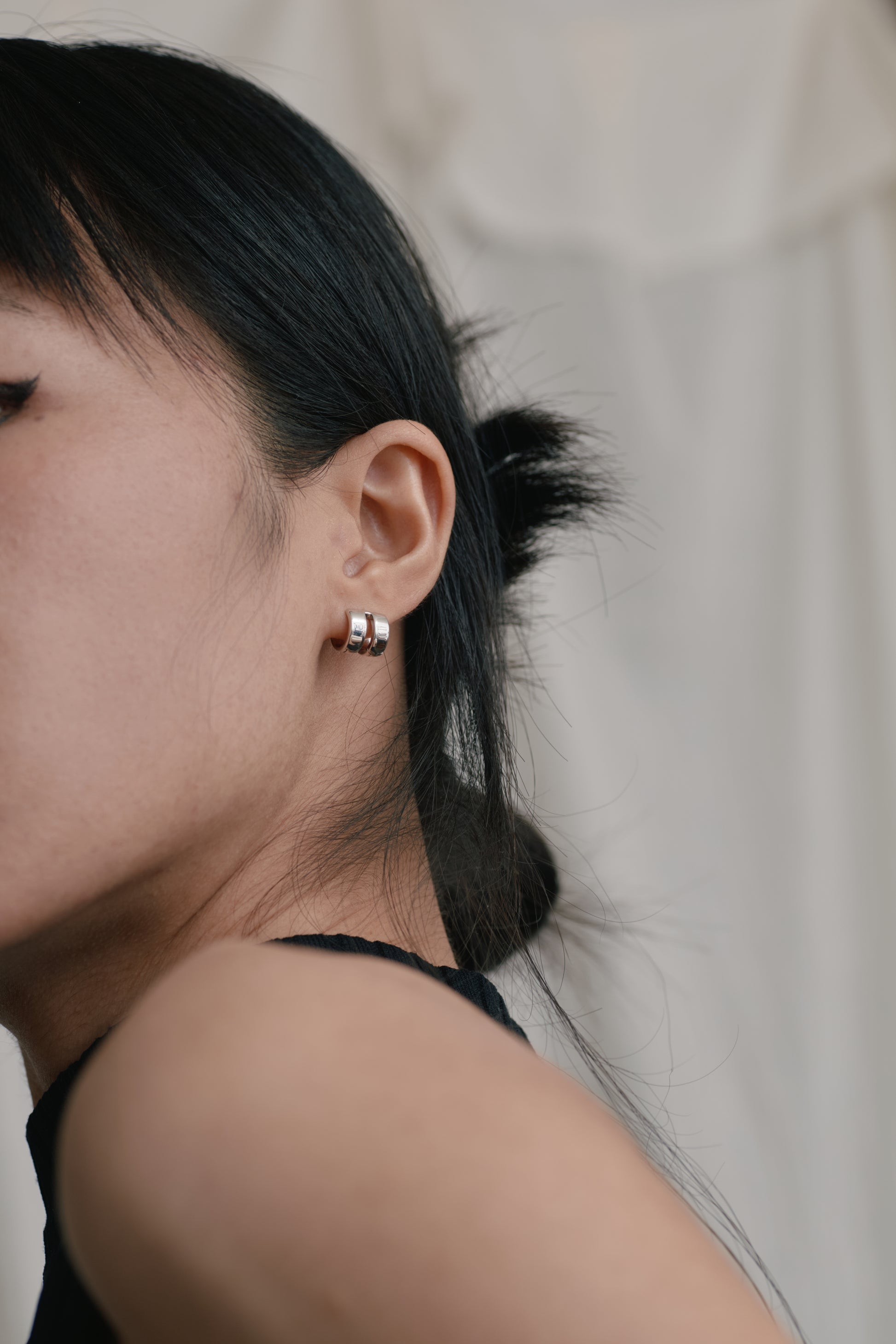 Close-up of a person wearing a small earring with a neutral background