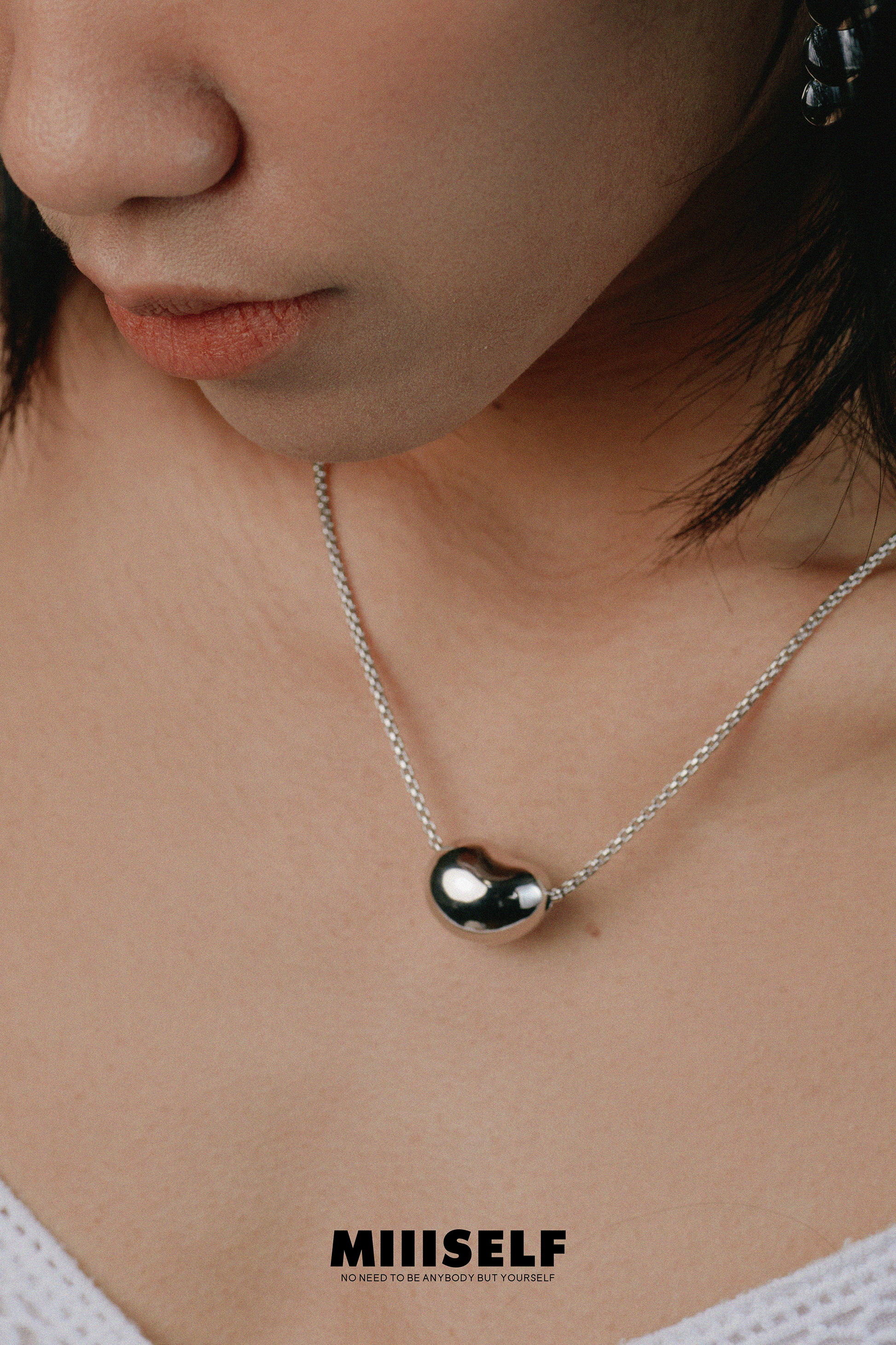 Close-up of a person wearing a necklace with a pendant, brand 'MIIISELF' visible.