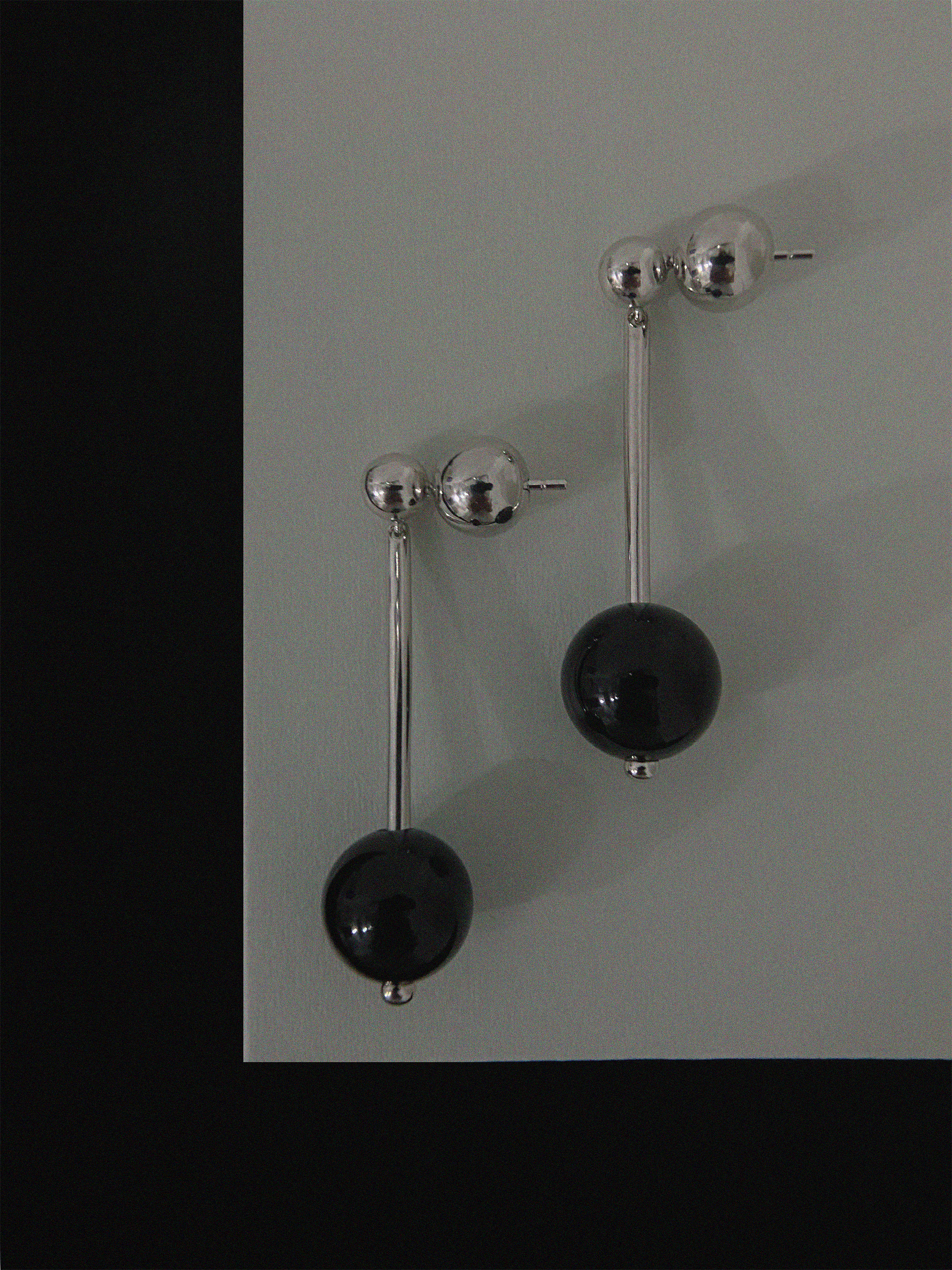 Pair of earrings with black spherical beads and silver bars on a gray background