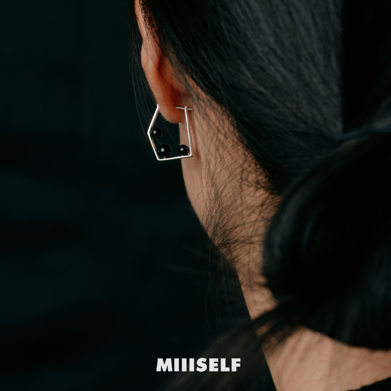 Close-up of an ear wearing a geometric earring with 'MIIISELF' branding.