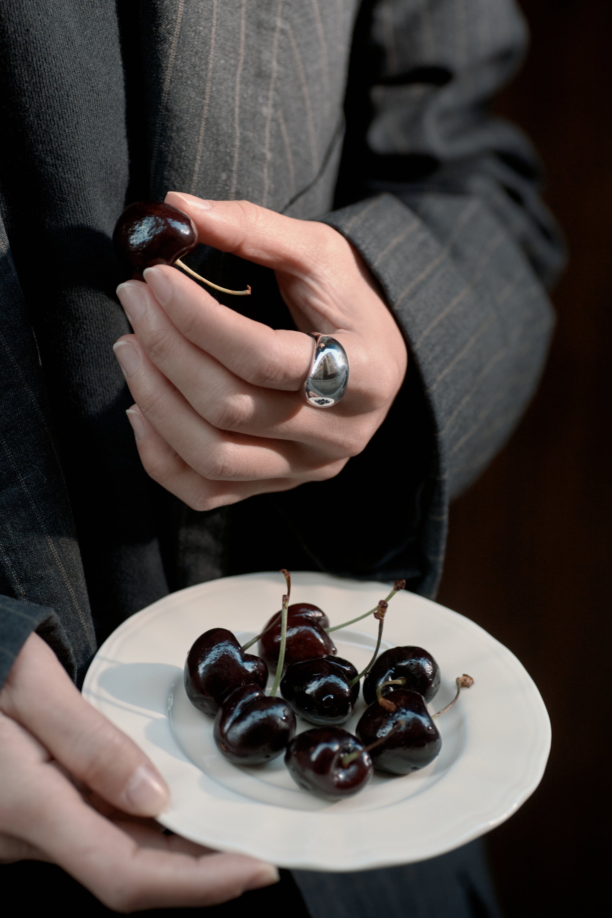 Person holding a plate of cherries with a close-up of their hand and a ring.
