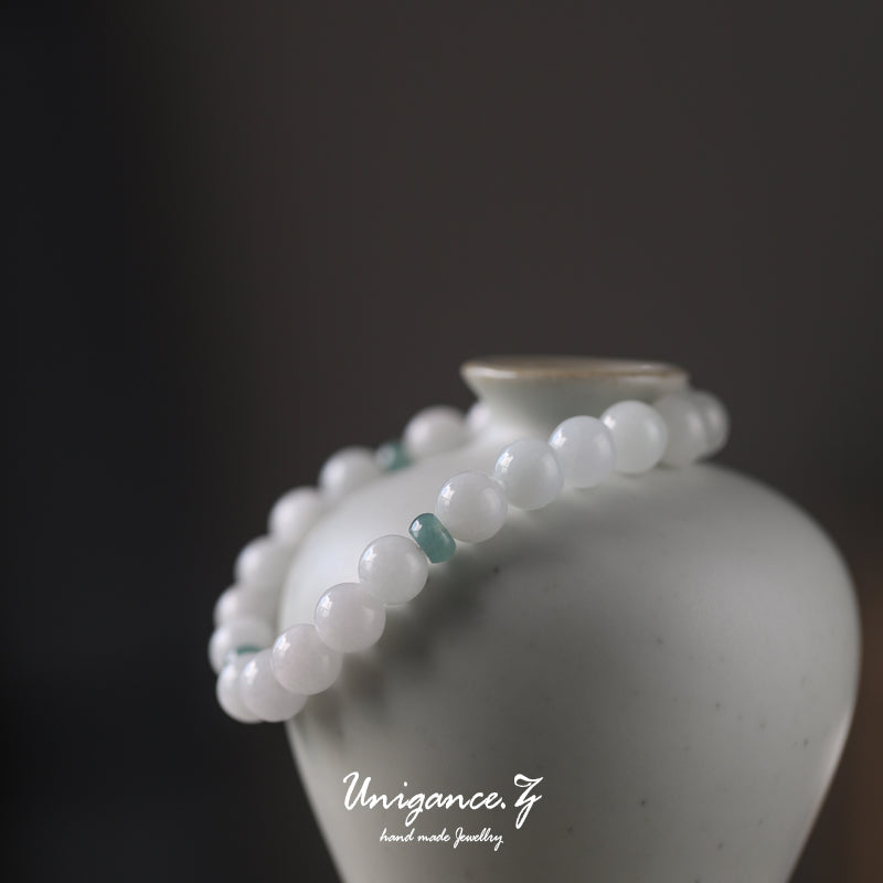 White beaded bracelet with green accents on a white vase against a dark background, featuring the brand 'Unigance'.