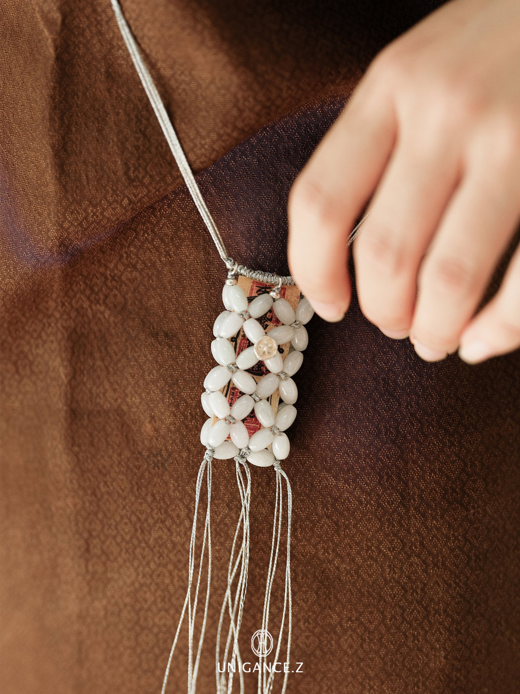 Close-up of a hand adjusting a beaded necklace on a brown fabric background