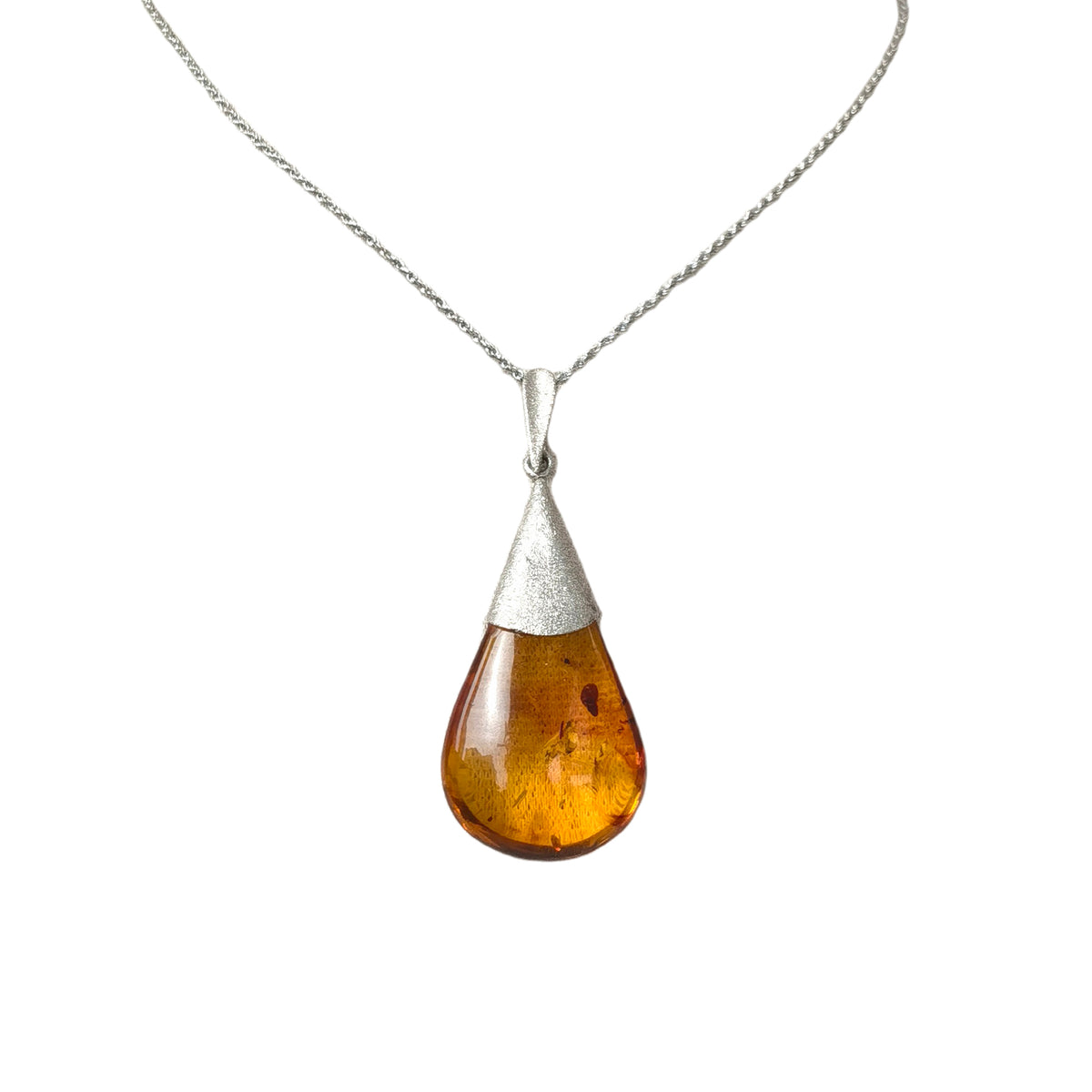 Natural Floral Amber & Matte Silver Necklace — Teardrop-shaped pendant with amber stone and silver top on a white background