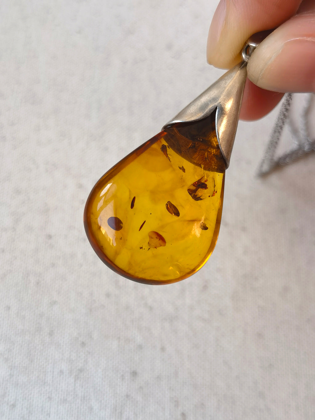 Natural Floral Amber & Matte Silver Necklace — Amber teardrop pendant with silver base held by a hand on a light background