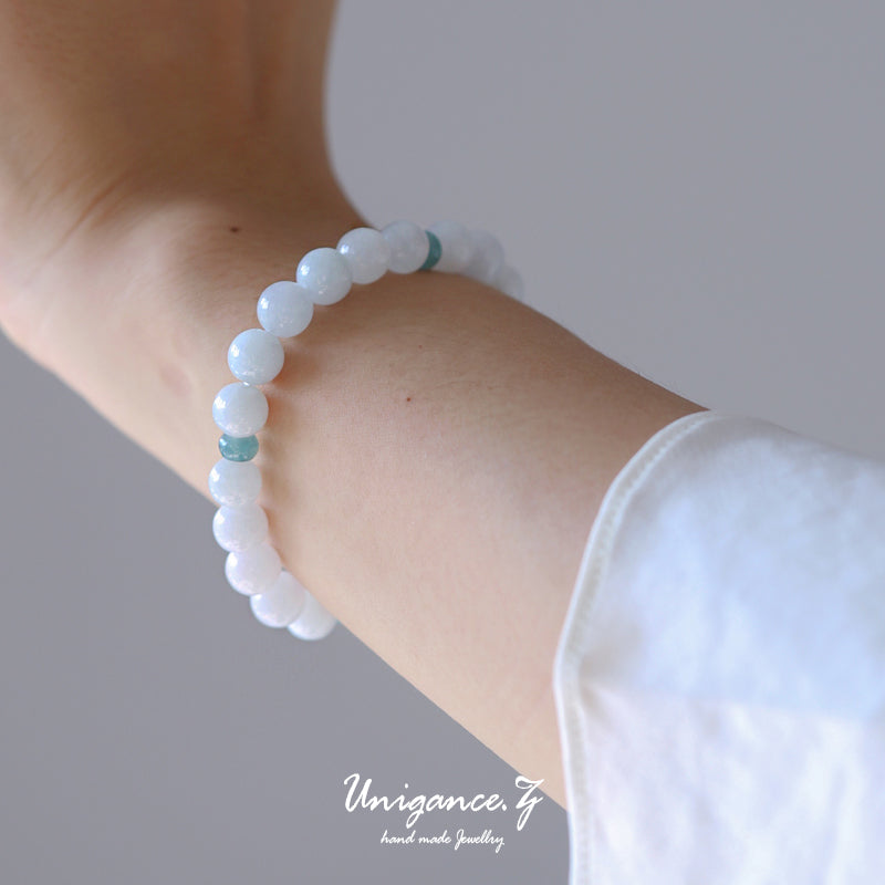 Close-up of a wrist wearing a white beaded bracelet with a plain background