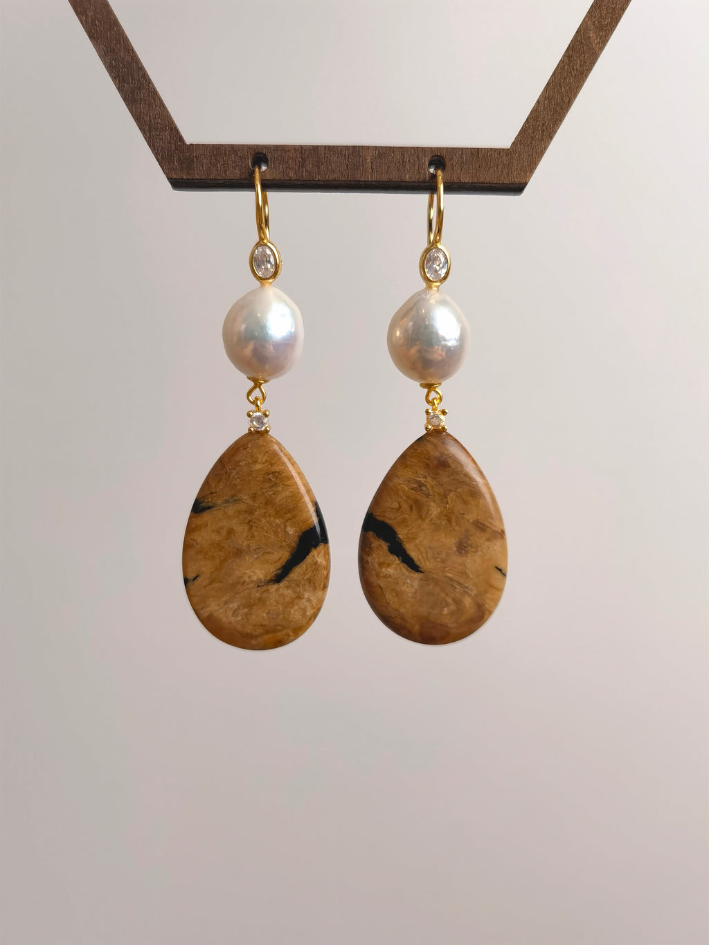 Natural Root Amber & Freshwater Pearl Earrings — Pair of earrings with teardrop-shaped stones and pearl beads on a light gray