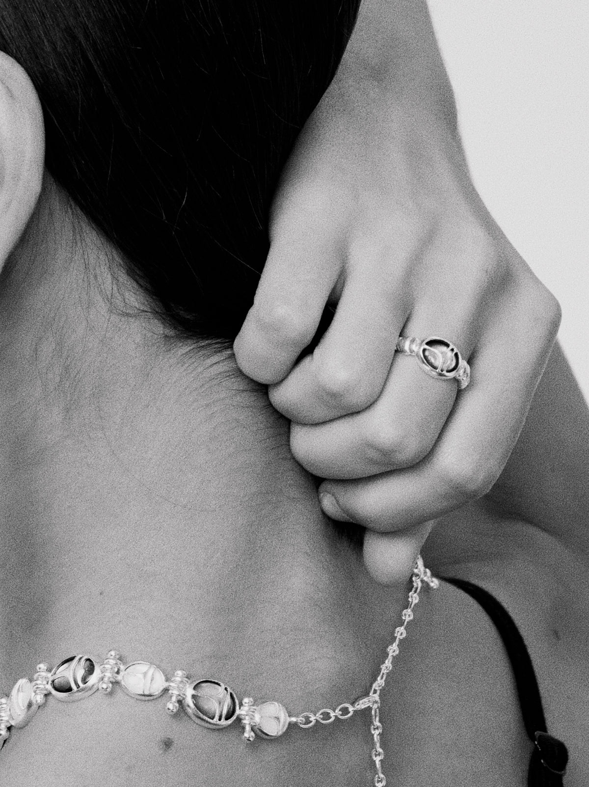 Nomadic Poem · Scarab Mother-of-Pearl Ouroboros Necklace — Close-up of a person wearing a ring and bracelet, with a blurred