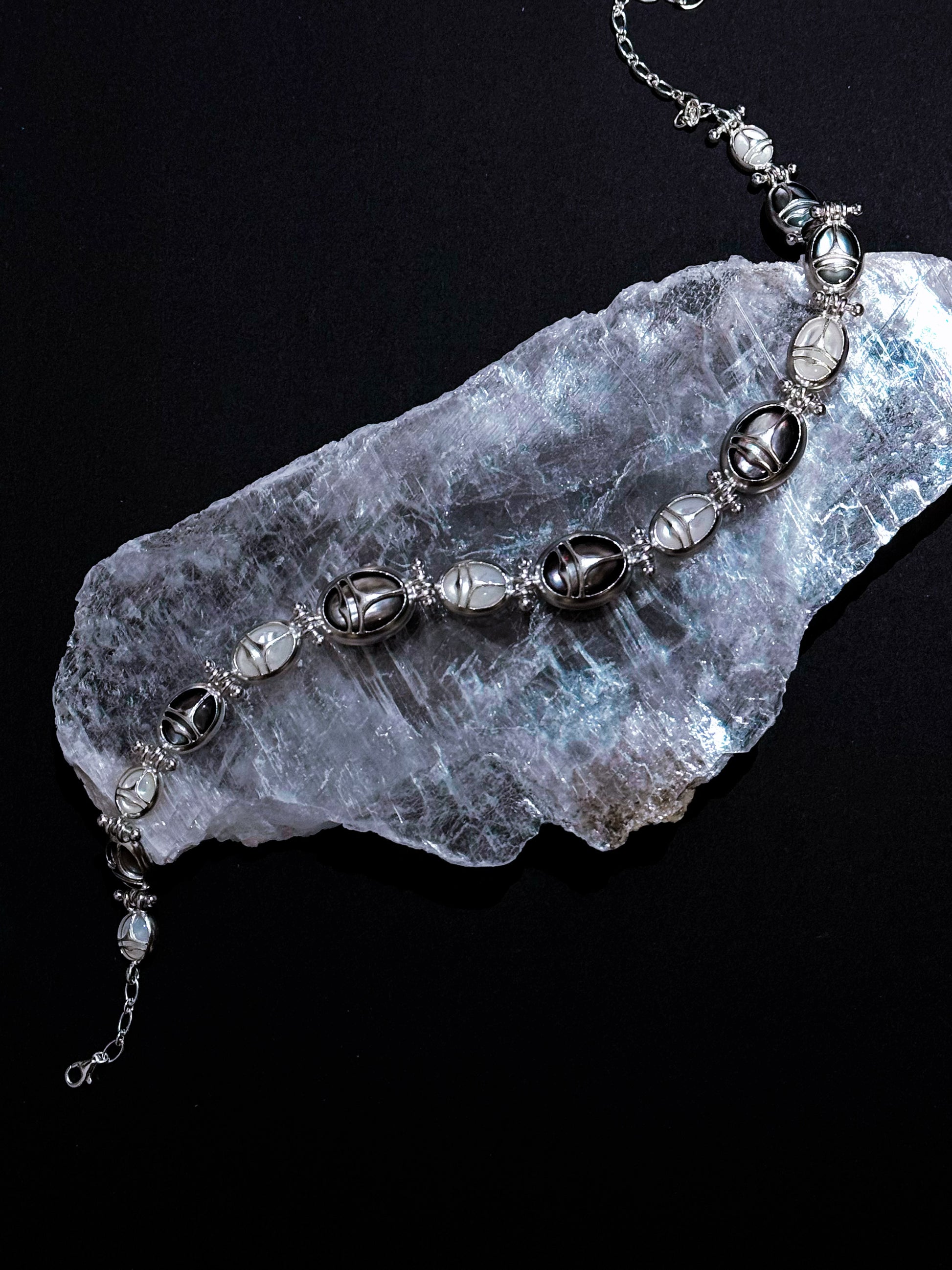 Nomadic Poem · Scarab Mother-of-Pearl Ouroboros Necklace — Silver beaded necklace on a clear crystal rock against a black