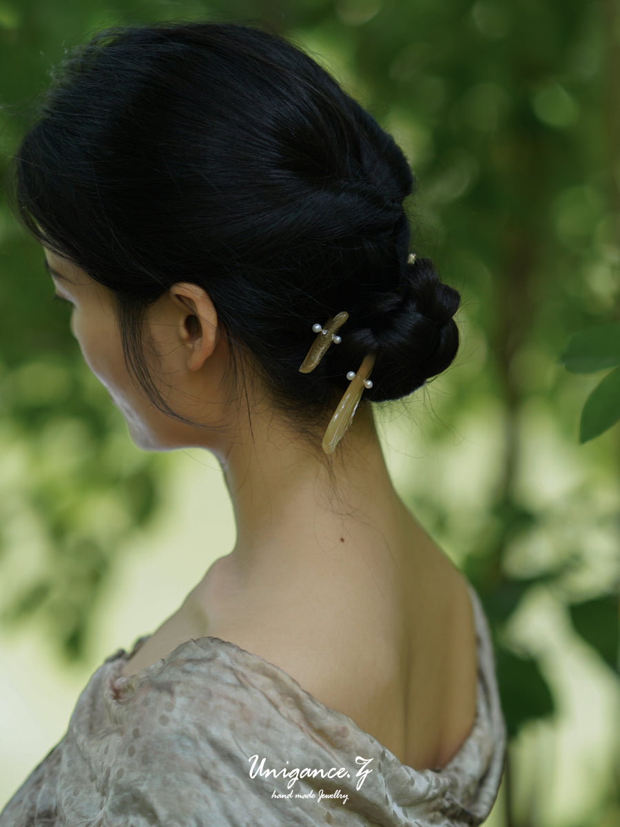 Woman with styled hair featuring a hairpin against a blurred green background