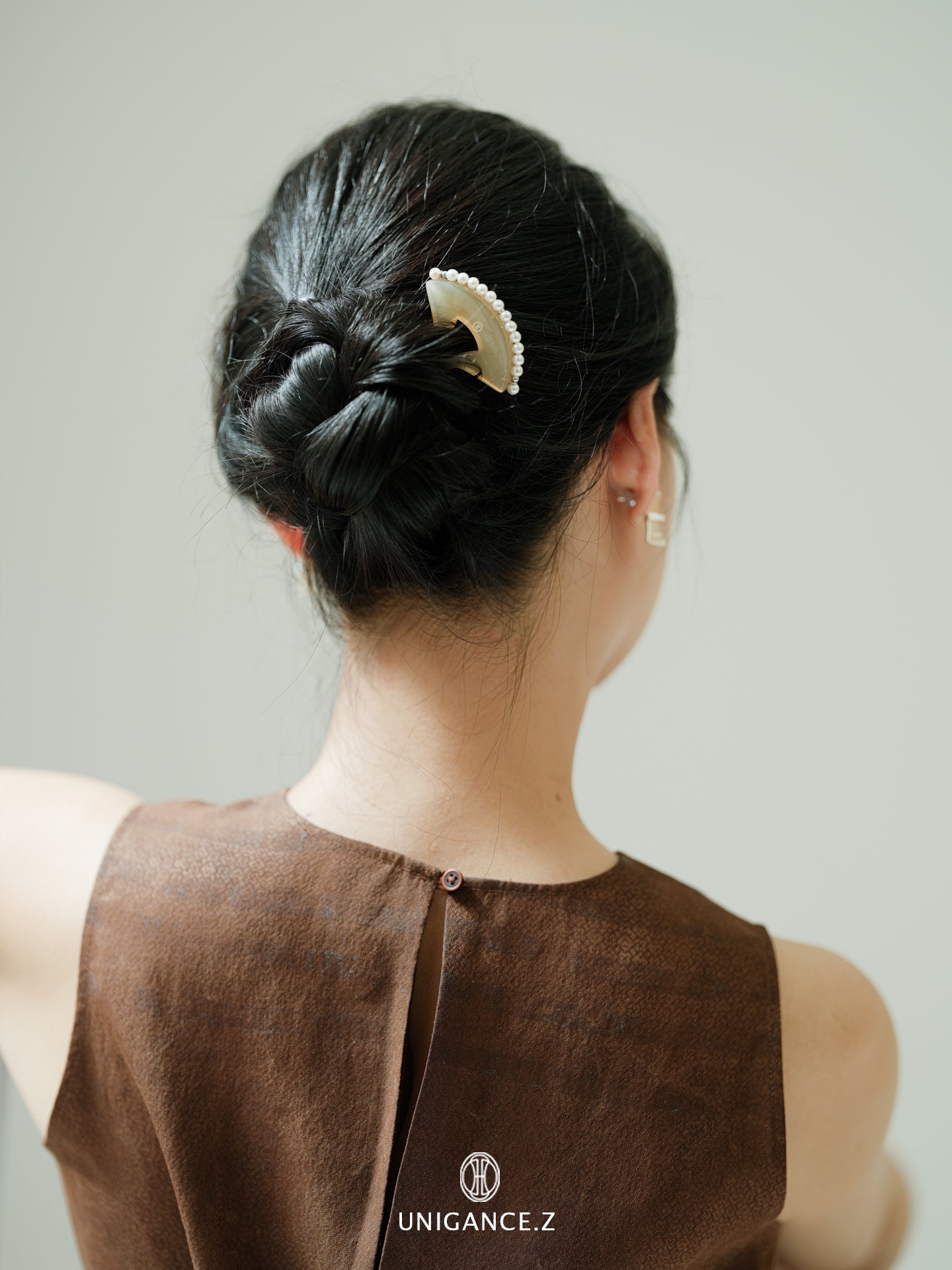 Person with a stylish hair bun wearing a brown top with 'UNIGANCE.Z' branding.