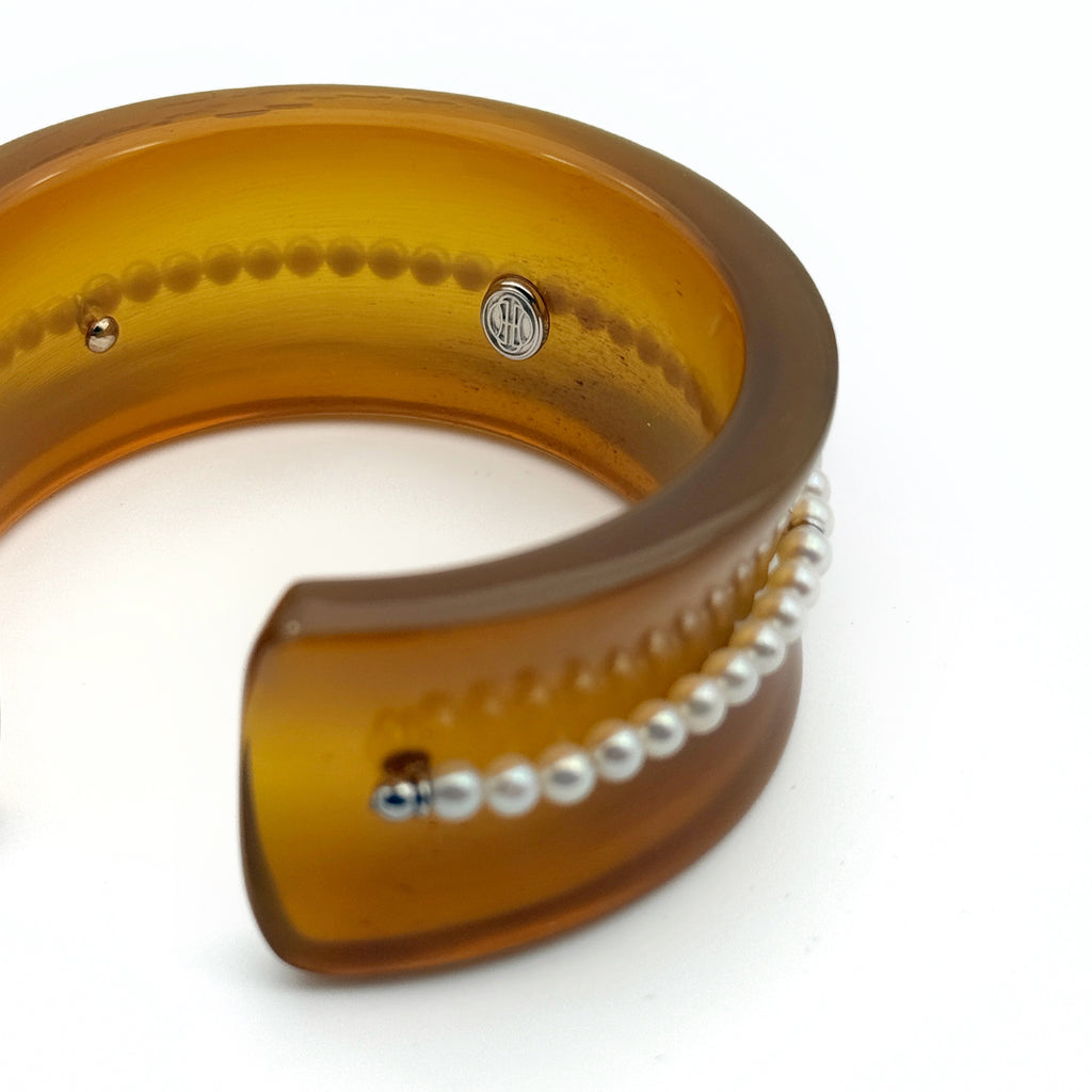 Pearl Inlay Open Cuff Horn Bracelet — Amber-colored bracelet with pearl-like beads on a white background