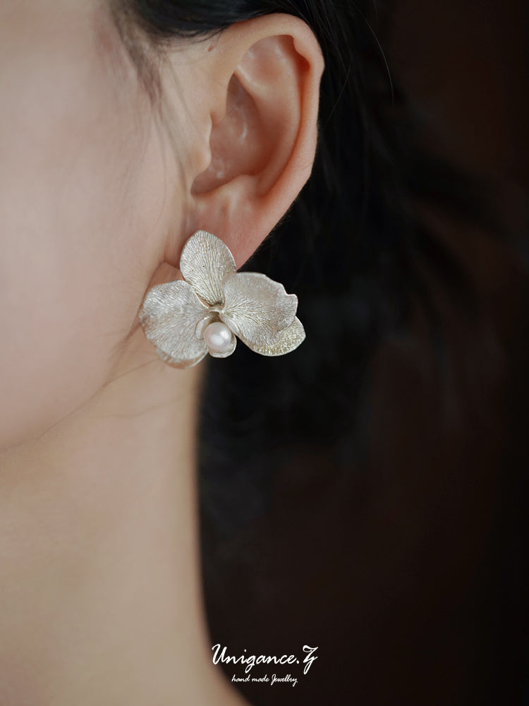 Phalaenopsis Orchid Convertible Earrings — Close-up of a person wearing a silver floral earring with a pearl accent, branded