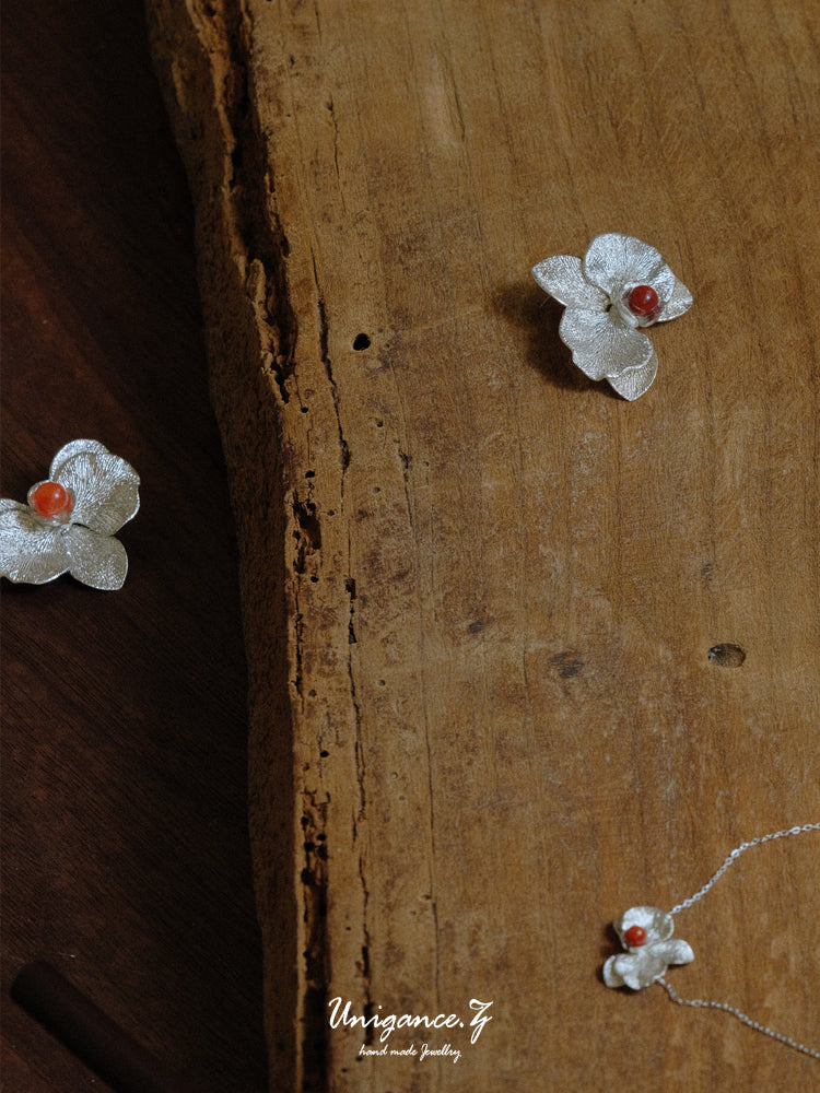 Phalaenopsis Orchid Convertible Earrings — Floral earrings with red centers on a wooden surface, featuring the brand