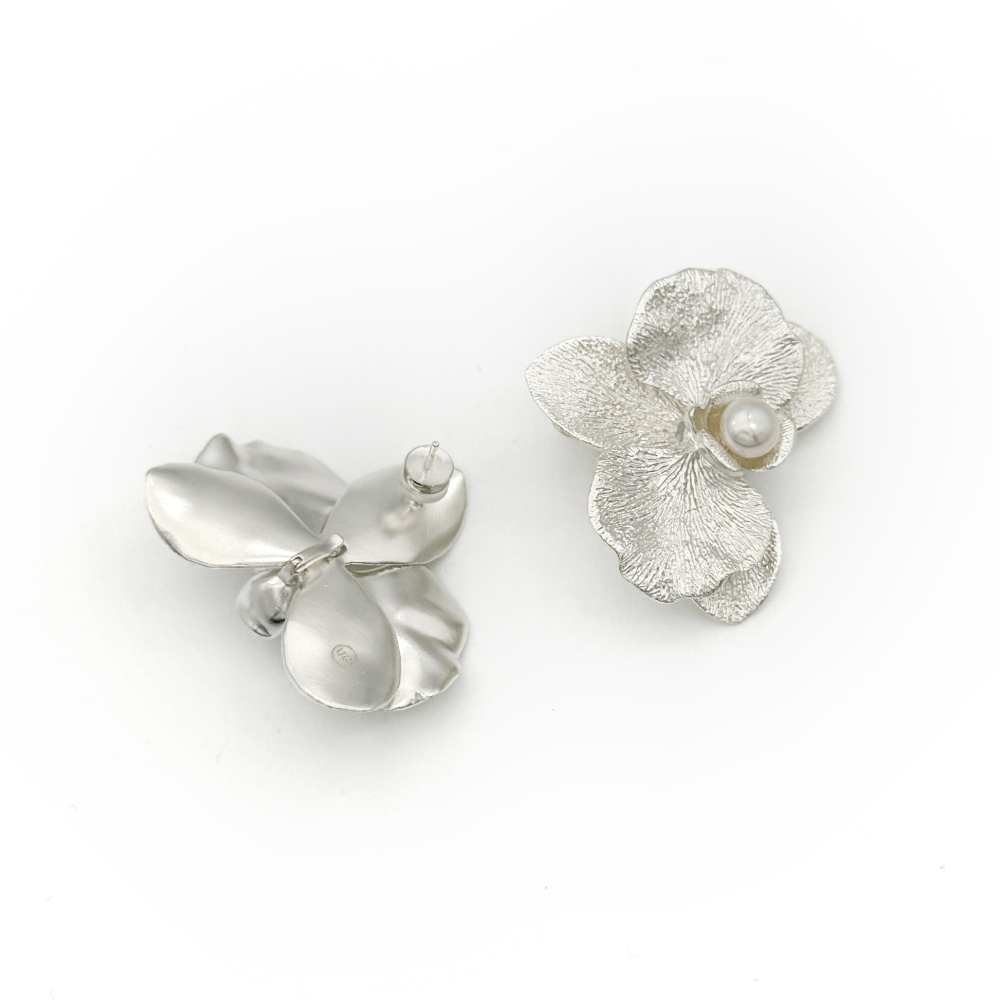 Silver flower-shaped earrings with a pearl on a white background