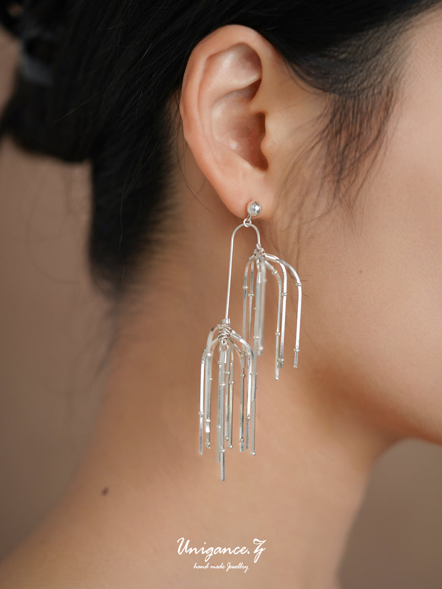 Pine Needle Drop Earrings — Silver earrings being worn on an ear with a blurred background