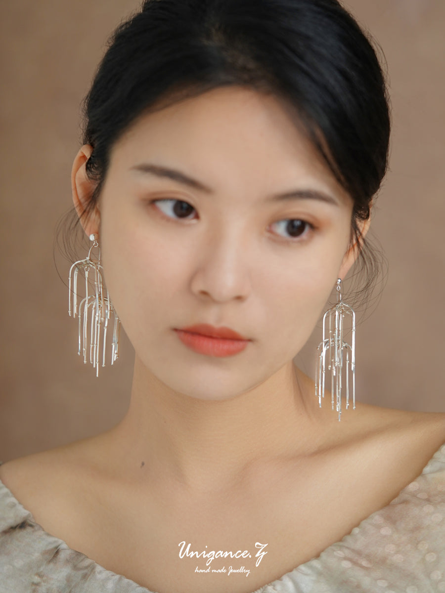 Pine Needle Drop Earrings — Woman wearing silver earrings with a blurred background