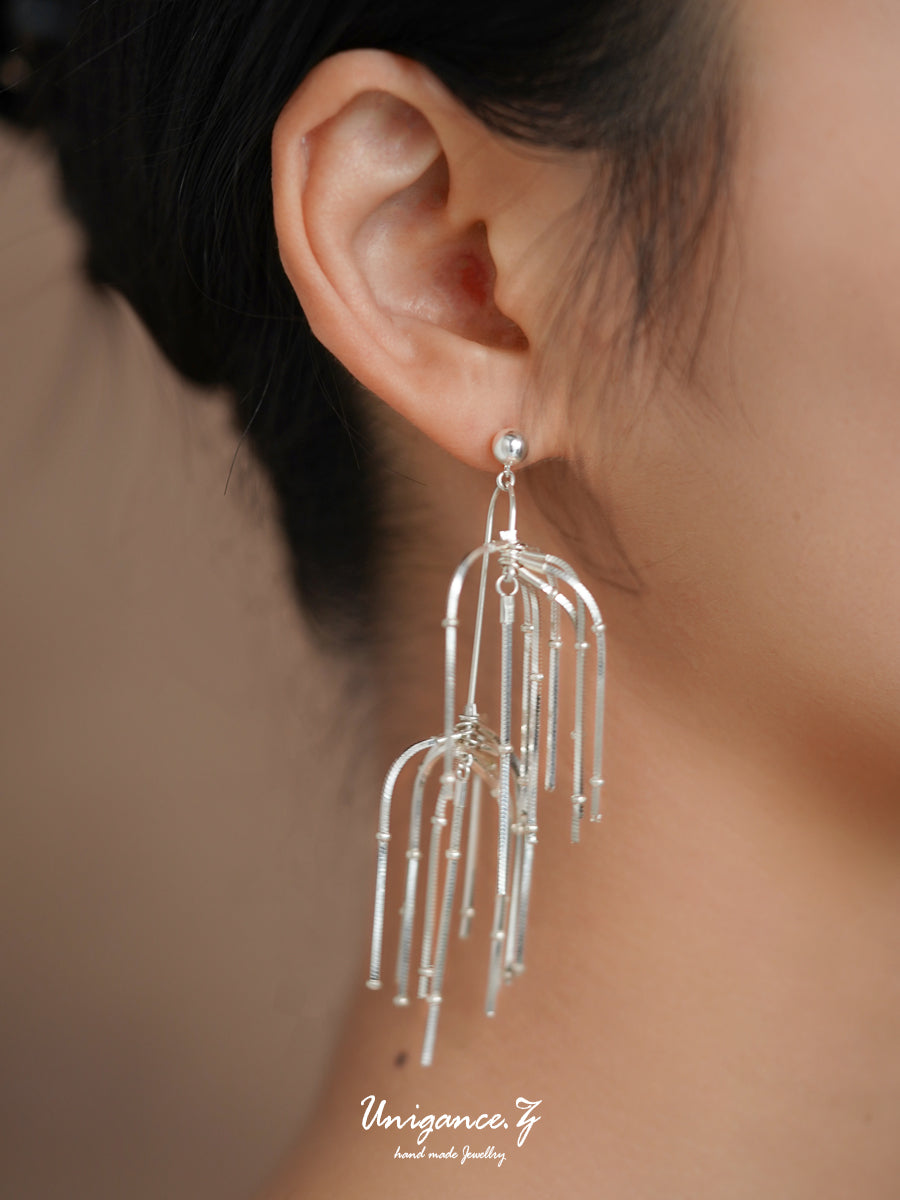 Pine Needle Drop Earrings — Silver earrings being worn with a blurred background