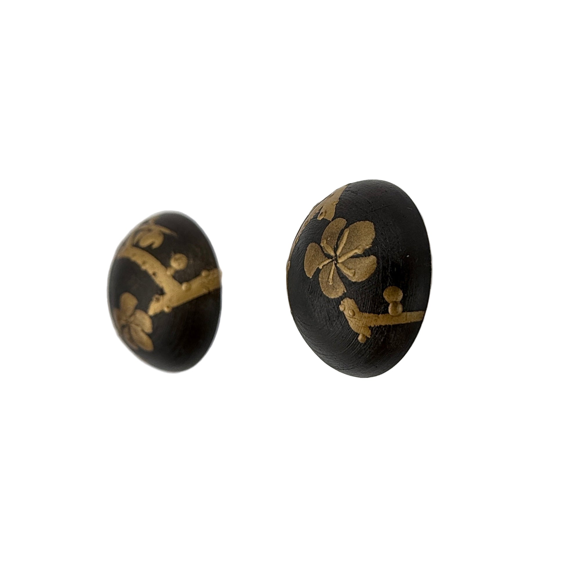 Black earrings with gold floral designs on a clear stand against a white background