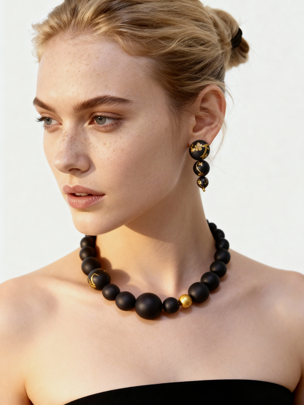 Plum Blossom Lacquer Quasi-Maki-e Earrings — Woman wearing a black and gold beaded necklace and earrings on a plain