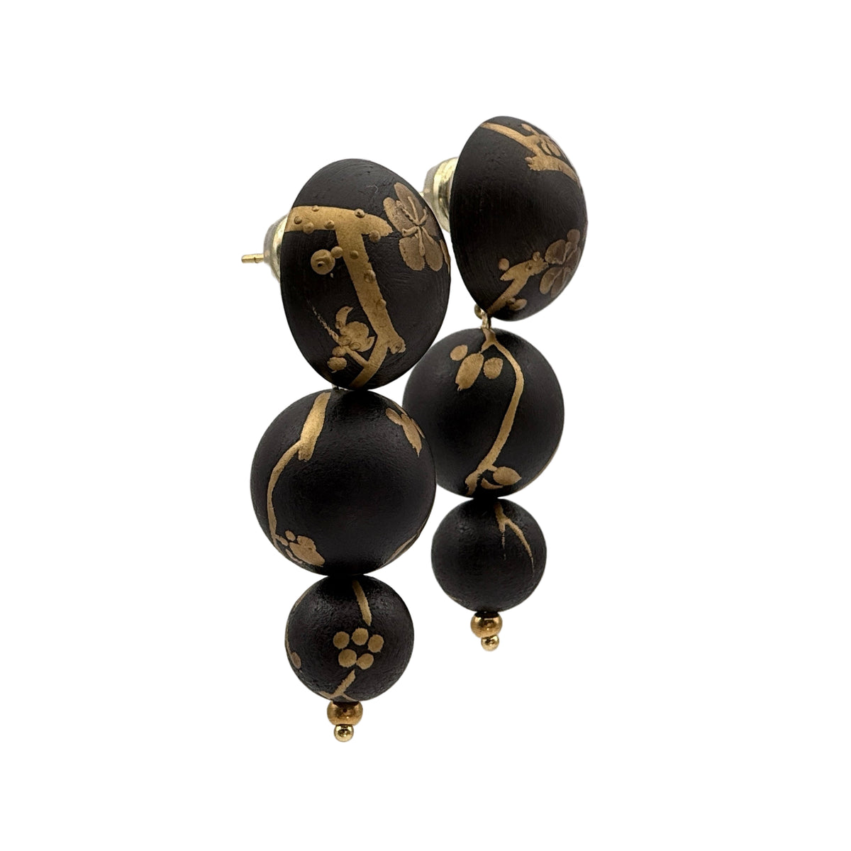 Plum Blossom Lacquer Quasi-Maki-e Earrings — Black earrings with gold designs on a clear stand